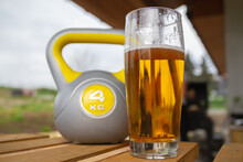 Glass Of Beer And Heavy Kettlebell Weight In Background. Contrasting Alcohol With Sports, Choice Between Healthy And Harmful Lifestyle. Cheat Day Temptation Vs Sticking To Diet.