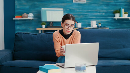 Wall Mural - Young adult talking on remote video call meeting at home, attending online school lesson on couch. University student using teleconference chat to discuss about education with teacher.