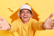 Portrait of kind pleased man wearing casual hoodie and panama looking through torn hole in yellow paper, giving free hugs with outstretched hands, welcoming inviting to embrace, support and care.