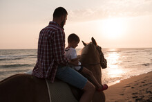 Father And Son Enjoy Riding Horses Together By The Sea. Selective Focus 
