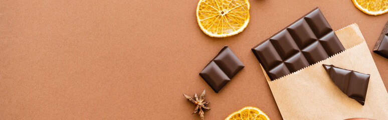 Wall Mural - Top view of anise, dry orange slice and chocolate in craft package on brown background, banner.