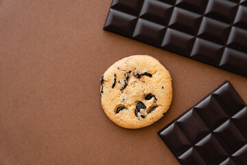 Wall Mural - Top view of cookie near dark chocolate bars on brown background.