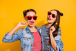 Photo of two funky positive girls lick lollipop candy enjoy free time isolated on yellow color background