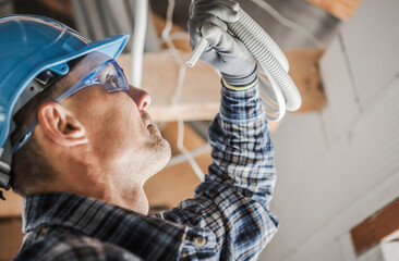 Wall Mural - Professional Electrician Closer Look. Caucasian Electric Worker Examining a Cable. Industrial Theme.