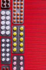 Wall Mural - top view of blister packs with different pills on crimson textured background.