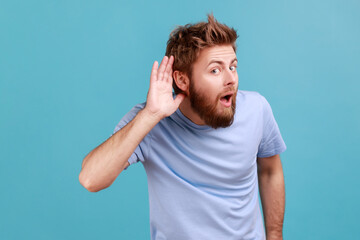 Can't hear you. Portrait of attentive bearded man holding hand near ear trying to listen quiet conversation, overhearing gossip, having hearing problems. Indoor studio shot isolated on blue background