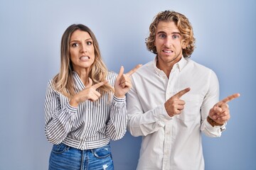 Poster - Young couple standing over blue background pointing aside worried and nervous with both hands, concerned and surprised expression