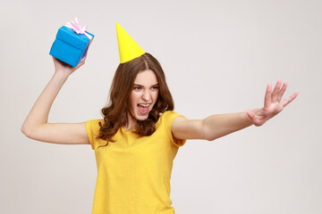 Poster - Catch your present! Take it! Happy carefree young female in yellow t-shirt ready to throw birthday box, having fun and sharing gift. Indoor studio shot isolated on gray background.