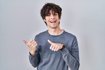 Sticker - Young man standing over isolated background pointing to the back behind with hand and thumbs up, smiling confident