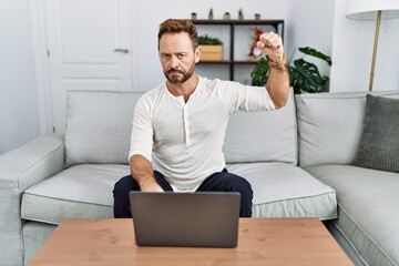 Sticker - Middle age man using laptop at home strong person showing arm muscle, confident and proud of power