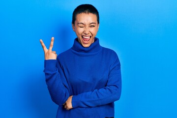 Poster - Beautiful hispanic woman with short hair wearing turtleneck sweater smiling with happy face winking at the camera doing victory sign. number two.