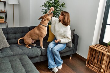 Poster - Young caucasian woman feeding dog sitting on sofa at home