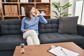 Poster - Young brunette woman at consultation office shouting and screaming loud to side with hand on mouth. communication concept.