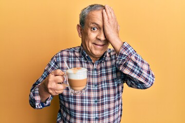 Canvas Print - Handsome senior man with grey hair drinking a cup coffee covering one eye with hand, confident smile on face and surprise emotion.