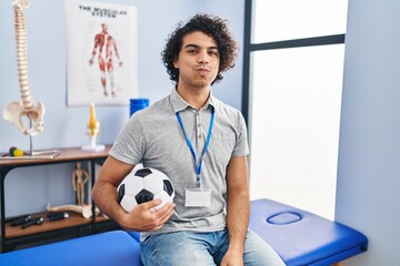 Canvas Print - Hispanic man with curly hair working as football physiotherapist puffing cheeks with funny face. mouth inflated with air, crazy expression.