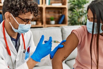 Young doctor man injecting covid-19 coronavirus vaccine for woman sitting on the sofa at the clinic.