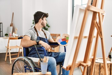 Sticker - Young hispanic man sitting on wheelchair painting at art studio looking to side, relax profile pose with natural face and confident smile.