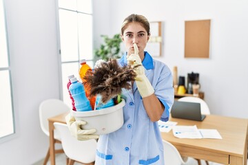 Sticker - Young blonde woman wearing cleaner uniform holding cleaning products asking to be quiet with finger on lips. silence and secret concept.