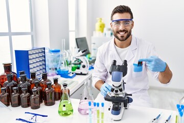 Canvas Print - Handsome hispanic man working at scientist laboratory smiling happy pointing with hand and finger