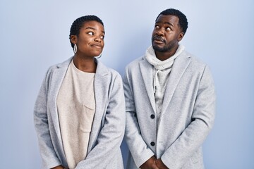 Sticker - Young african american couple standing over blue background together smiling looking to the side and staring away thinking.