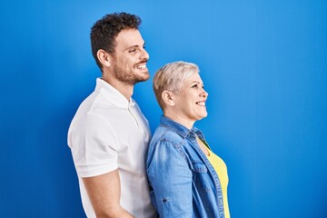 Poster - Young brazilian mother and son standing over blue background looking to side, relax profile pose with natural face and confident smile.