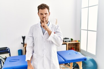 Wall Mural - Handsome young man working at pain recovery clinic asking to be quiet with finger on lips. silence and secret concept.