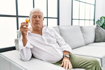 Poster - Senior man holding pills relaxed with serious expression on face. simple and natural looking at the camera.