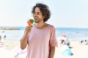 Canvas Print - Young hispanic man smiling happy eating ice cream at the beach.