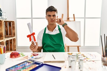 Poster - Young hispanic man at art studio holding degree mouth and lips shut as zip with fingers. secret and silent, taboo talking