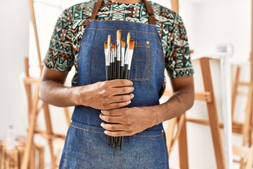 Sticker - Young african american artist man holding paintbrushes at art studio.