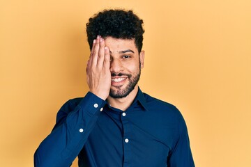 Poster - Young arab man with beard wearing casual shirt covering one eye with hand, confident smile on face and surprise emotion.