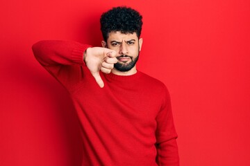 Sticker - Young arab man with beard wearing casual red sweater looking unhappy and angry showing rejection and negative with thumbs down gesture. bad expression.