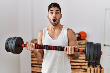 Sticker - Young hispanic man training with weighs afraid and shocked with surprise and amazed expression, fear and excited face.