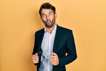 Poster - Handsome man with beard wearing business suit holding jacket making fish face with mouth and squinting eyes, crazy and comical.