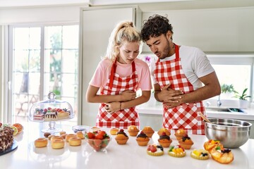 Sticker - Couple of wife and husband cooking pastries at the kitchen with hand on stomach because nausea, painful disease feeling unwell. ache concept.