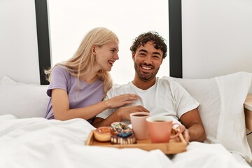 Poster - Young beautiful couple smiling happy having breakfast on the bed at home.