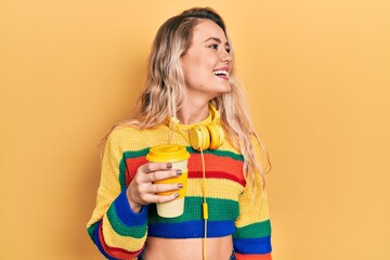 Sticker - Beautiful young blonde woman drinking cup of coffee wearing headphones looking away to side with smile on face, natural expression. laughing confident.