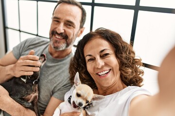 Poster - Middle age hispanic couple smiling happy making selfie by the camera. Lying on the bed with dogs at home.