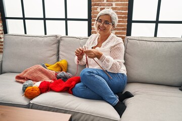 Middle age woman weaving in ends sitting on sofa at home