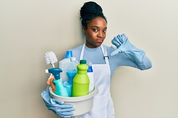 Poster - African american woman with braided hair wearing apron holding cleaning products with angry face, negative sign showing dislike with thumbs down, rejection concept