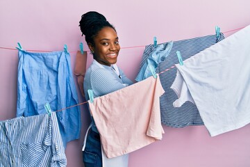 Poster - African american woman with braided hair washing clothes at clothesline pointing aside with hands open palms showing copy space, presenting advertisement smiling excited happy