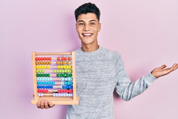 Young hispanic man holding traditional abacus celebrating achievement with happy smile and winner expression with raised hand