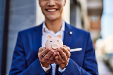 Young man wearing suit holding piggy bank at street