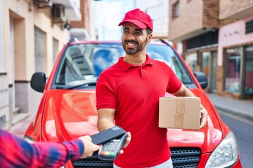 Canvas Print - Young hispanic man courier charging with dataphone and smartphone at street