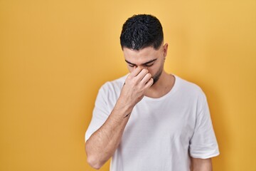 Wall Mural - Young handsome man wearing casual t shirt over yellow background tired rubbing nose and eyes feeling fatigue and headache. stress and frustration concept.