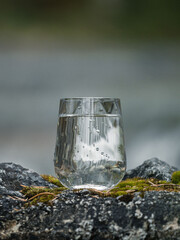 Sticker - Closeup shot of a glass cup of water on a rocky surface reflecting a rounf with blurred background