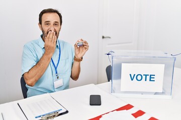 Poster - Middle age man with beard sitting by ballot holding i vote badge laughing and embarrassed giggle covering mouth with hands, gossip and scandal concept