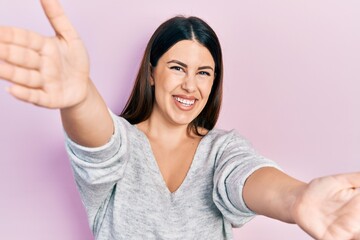 Poster - Young hispanic woman wearing casual clothes looking at the camera smiling with open arms for hug. cheerful expression embracing happiness.