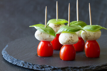 Caprese sticks with mozzarella, tomatoes and basil leaves on black background