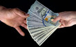 © Mariia Human - Hand-to-hand cash exchange: dollars on a black background
